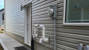 Un edificio con tuberías exteriores, una puerta, una ventana y una acera de hormigón.