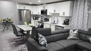 Una cocina moderna con armarios blancos, un comedor con mesa de mármol y un sofá de cuero negro con cojines estampados.