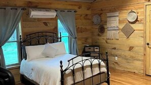 Une chambre dans une cabane en bois, avec un lit, un ventilateur de plafond et une fenêtre avec des rideaux.