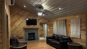 L’intérieur d’une cabane en rondins, avec une cheminée, un canapé en cuir et un téléviseur à écran plat fixé au mur.