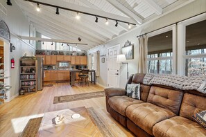 Ein großzügiges Wohnzimmer mit braunem Ledersofa, einem Couchtisch und einem Kamin. Es gibt eine Küchenzeile mit Holzschränken und einem Esstisch.