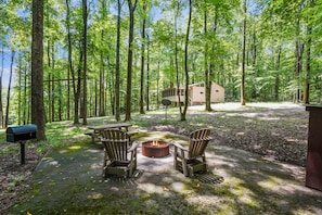 Een bebost gebied met een vuurplaats, Adirondack-stoelen, een klein vakantiehuisje en een brievenbus.