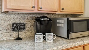 A kitchen with wooden cabinets, a coffee maker, a microwave, and two mugs with 'MERRY BRIGHT' text.