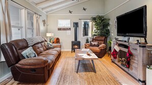 A cozy living room with a leather sofa, a fireplace, a television, and a ceiling fan. - Woodland Cottage | Secluded Hocking Hills Getaway (Laurelville)