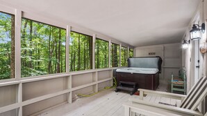 A room with a hot tub, wooden deck, and large windows overlooking a forest. - Woodland Cottage | Secluded Hocking Hills Getaway (Laurelville)
