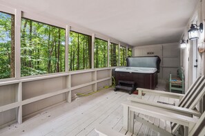 Eine Holzterrasse mit Whirlpool, einer Holzbank und Blick auf einen Wald durch große Fenster.