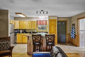 Une cuisine avec des meubles de rangement en bois, un îlot central doté de tabourets, un réfrigérateur et un four à micro-ondes.