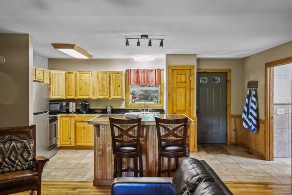 A kitchen with wooden cabinets, a central island with stools, a refrigerator, and a microwave.