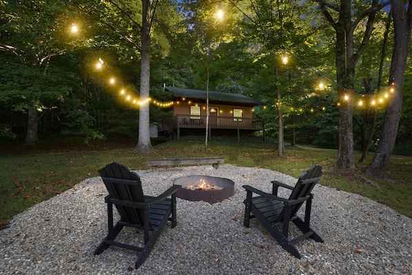 A cabin with a deck, surrounded by trees, and a fire pit with two chairs in front. - Outback Cabin | Hocking Hills, Cozy Cabin for 2 (Laurelville)