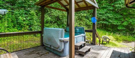 A wooden deck with a hot tub and a covered seating area surrounded by lush greenery.