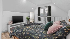 Et soveværelse med en seng, et fjernsyn, en plante og et vindue med gardiner.