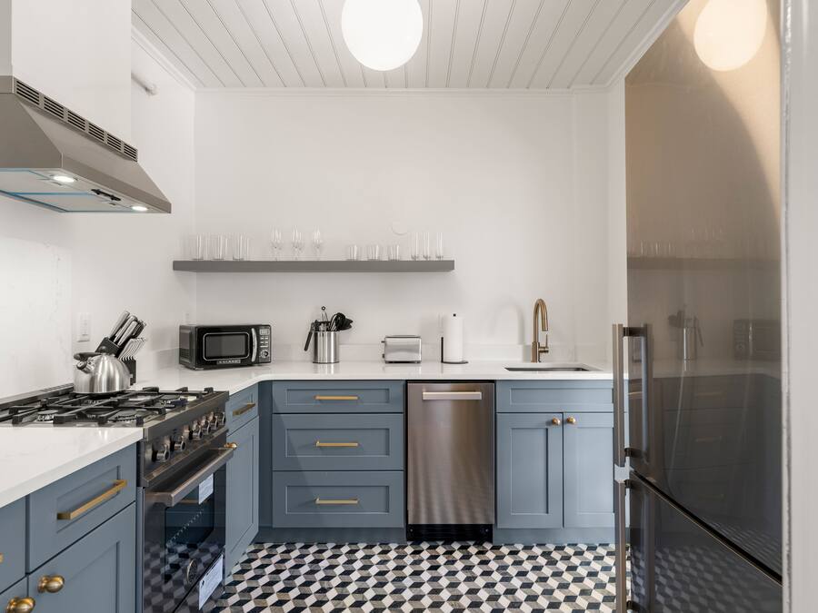 A modern kitchen with grey cabinets, stainless steel appliances, and a checkered floor.