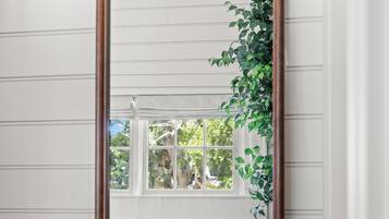 Ein Spiegel mit Holzrahmen, der einen Raum mit weißen Wänden, einem Fenster und einer Pflanze reflektiert.