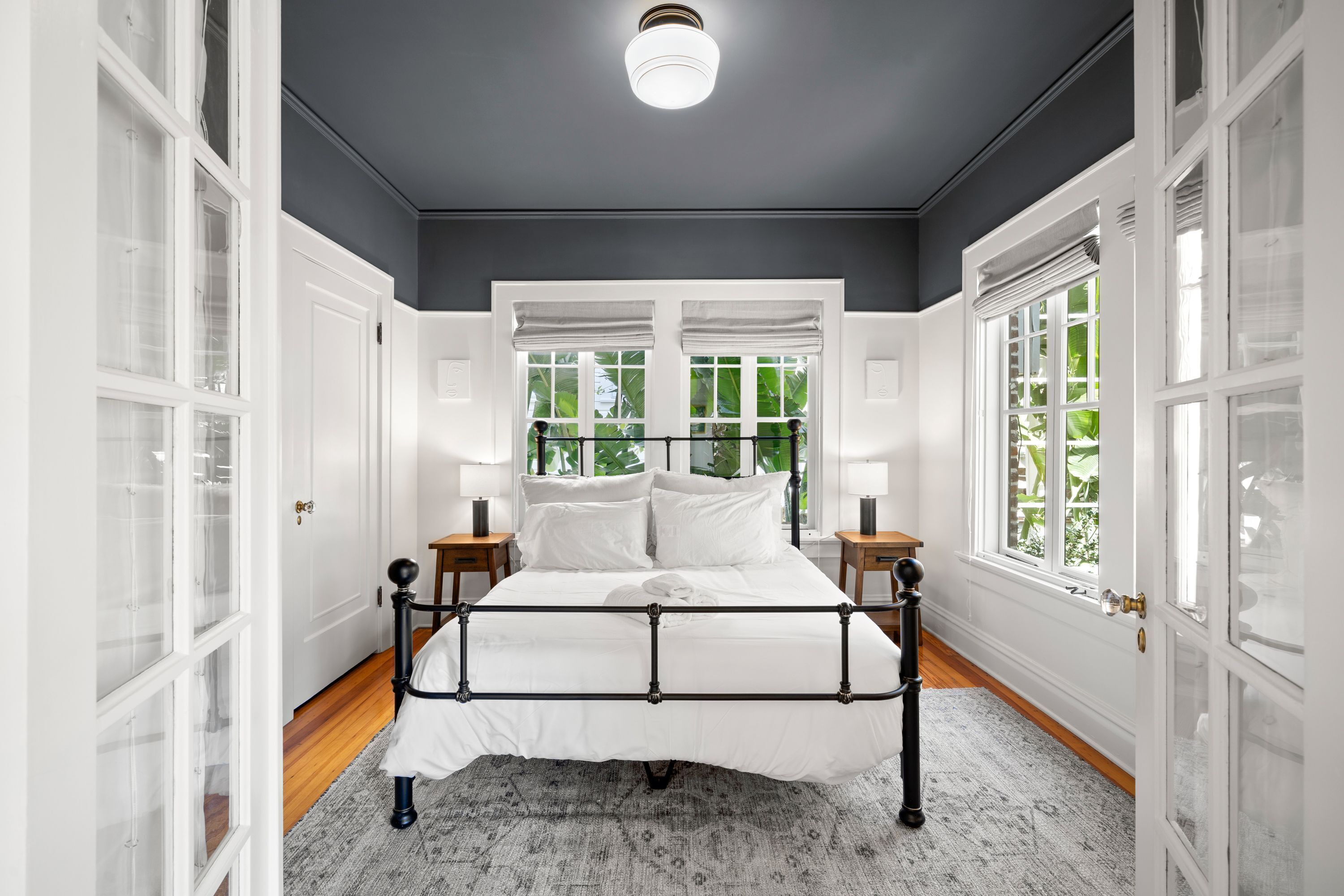 Ein Schlafzimmer mit Bett, weißen Wänden und großen Fenstern.