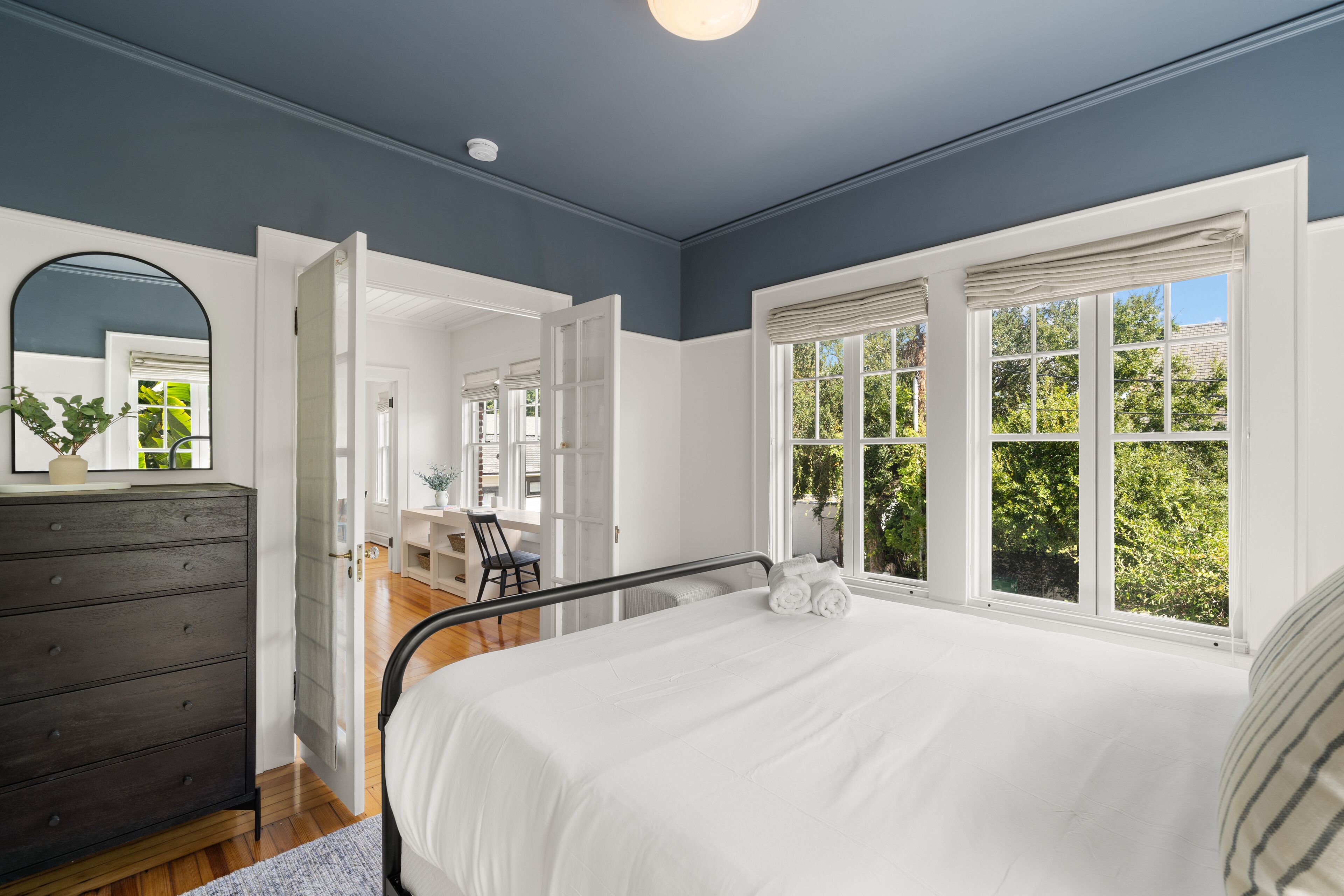 A bedroom with a bed, dresser, and a view of greenery outside.