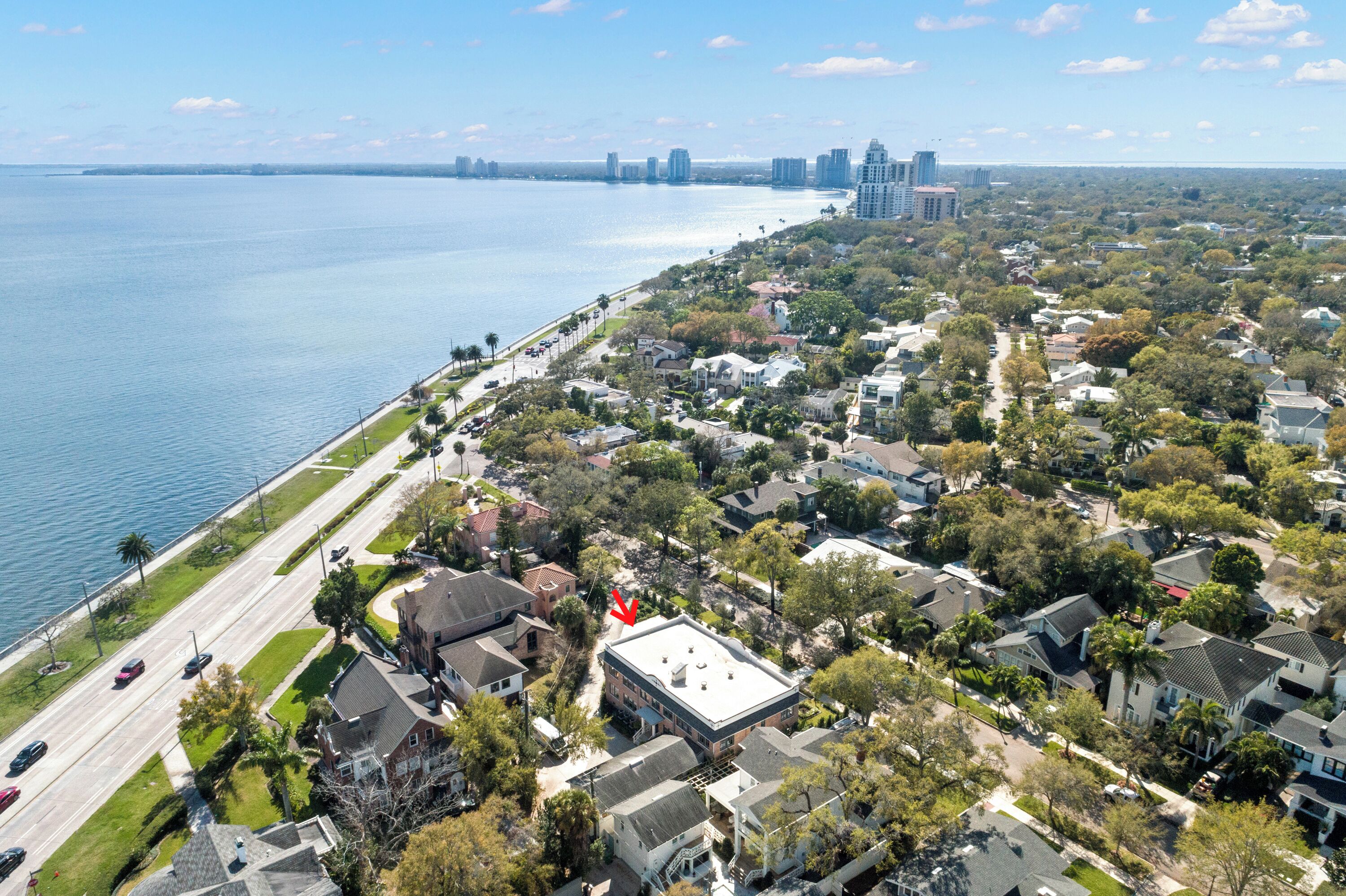 An aerial view of a coastal residential area with houses, a road, and a body of water.