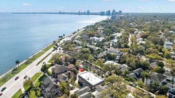 An aerial view of a coastal residential area with houses, a road, and a body of water.