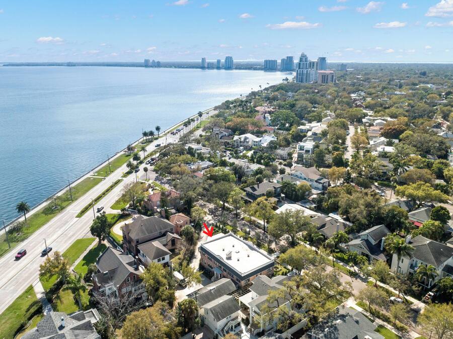 An aerial view of a coastal residential area with houses, a road, and a body of water.
