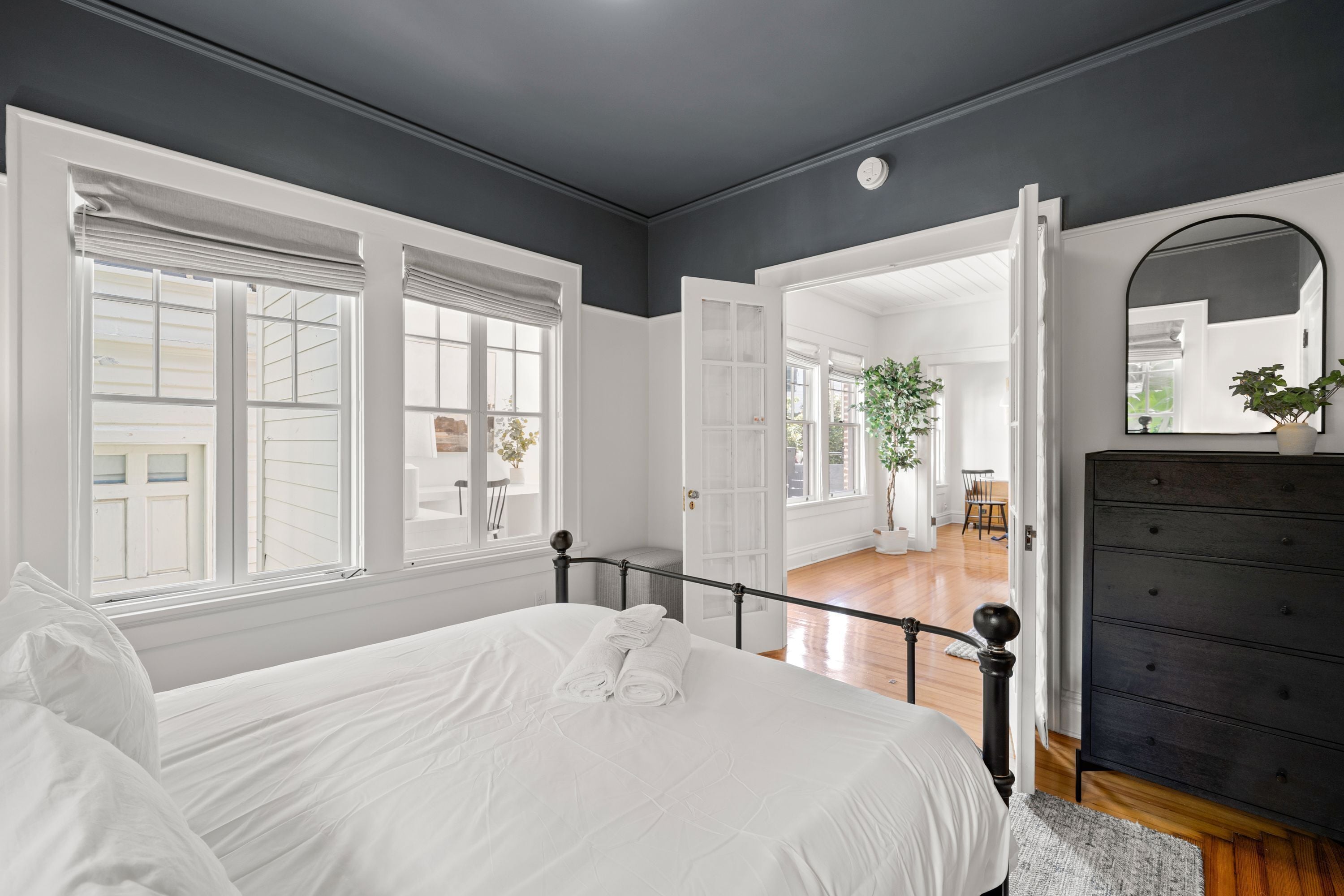 A bedroom with a large bed, white bedding, a dark dresser, and a mirror.