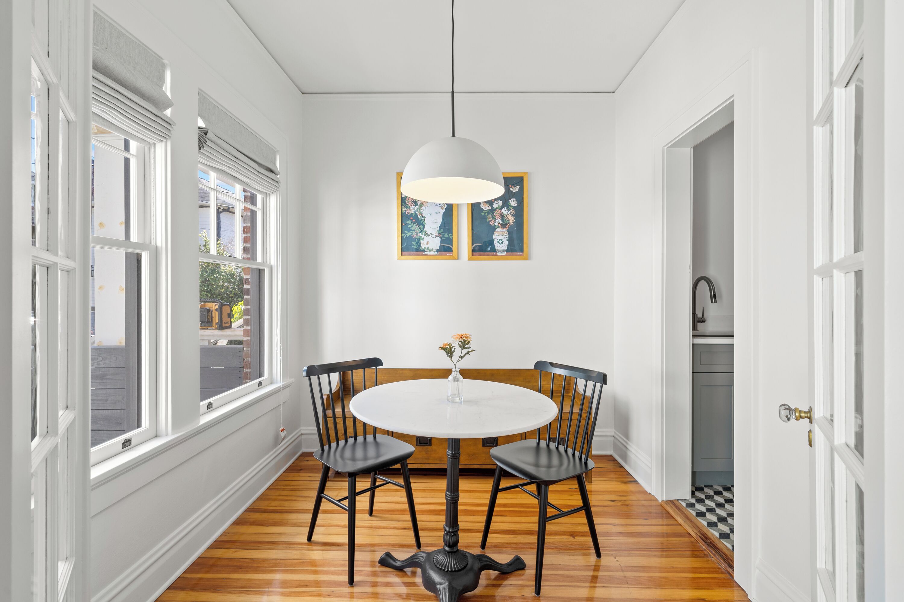 Un coin repas comprenant une table ronde, quatre chaises, un luminaire suspendu et deux tableaux encadrés accrochés au mur.