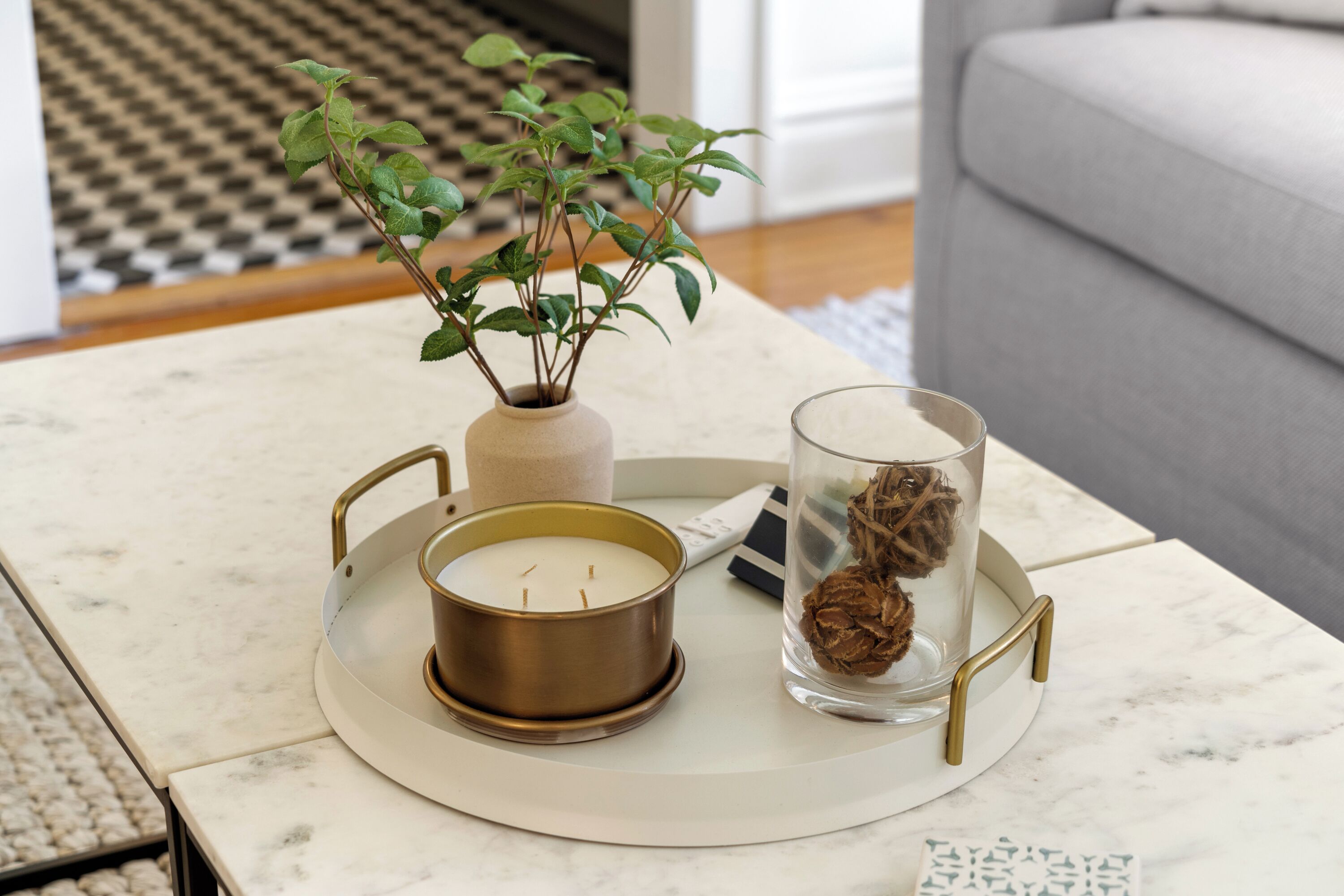 A marble table with a candle, a vase with a plant, and a glass container with dried flowers.