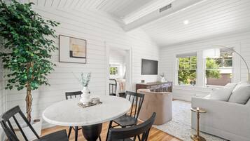 A modern living room with a round dining table, dark wooden chairs, a white sofa, and a large potted plant.