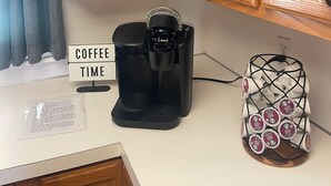 A kitchen with a coffee maker, a cabinet with various items, and a coffee pod holder.