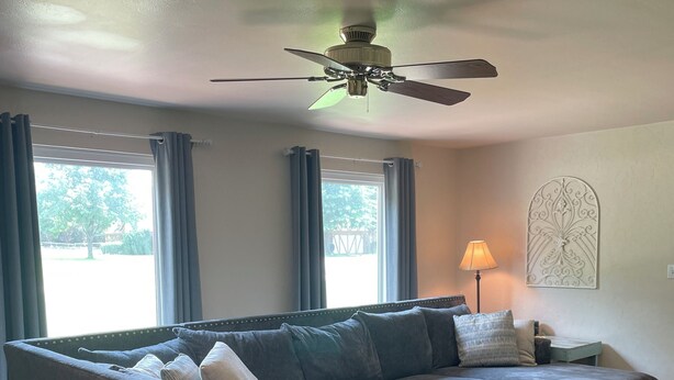 A modern living room with a sectional sofa, a ceiling fan, a lamp, and a decorative wall piece.