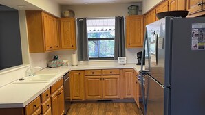 A kitchen with wooden cabinets, a stainless steel refrigerator, a window with curtains, and a skylight.