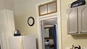 Une cuisine équipée d’un réfrigérateur, d’un évier et de placards. Il y a une horloge au mur et un ventilateur de plafond.