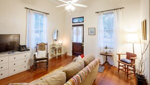 Un salon comprenant un canapé, des fauteuils, un téléviseur, un ventilateur de plafond et une porte ornée d’un vitrail.
