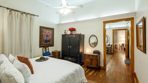 Une chambre avec un grand lit, un plancher en bois, un ventilateur de plafond, une armoire et un miroir.