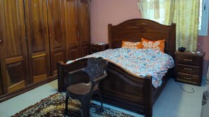 A bedroom with a wooden bed, a nightstand, a chair, a wardrobe, and a window with curtains.
