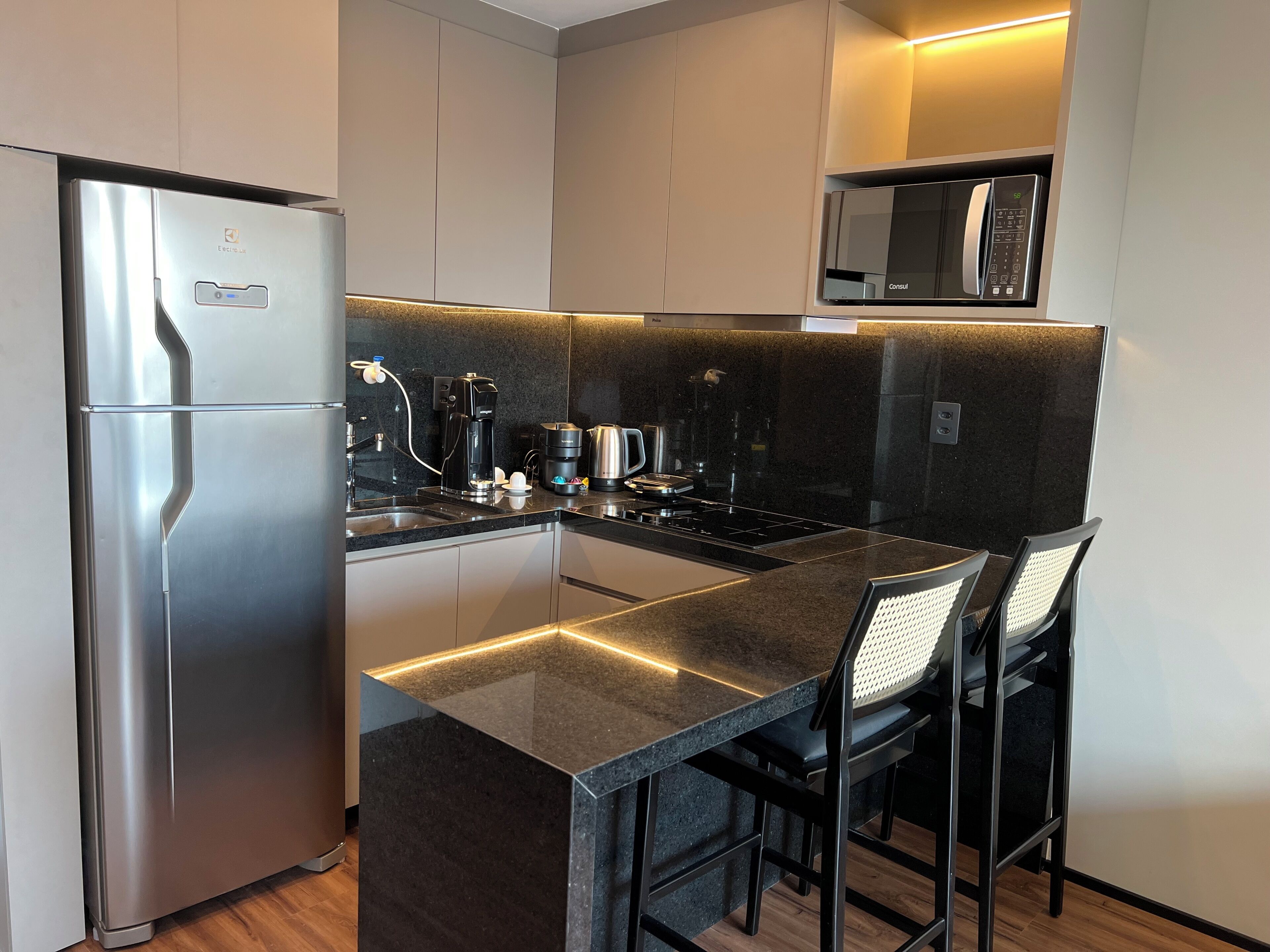 Eine moderne Küche mit Edelstahlkühlschrank, integriertem Mikrowellenherd, Kaffeemaschine und einer Bar mit Sitzgelegenheiten.