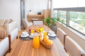 A dining area with a wooden table, white chairs, a potted plant, and a city view.