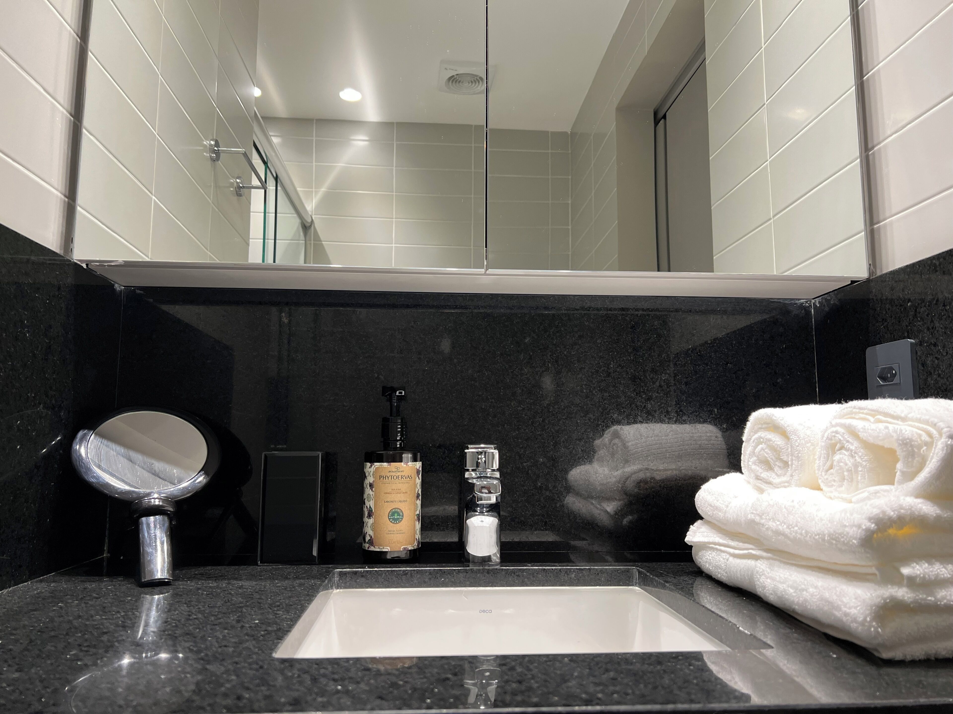 A bathroom with a sink, mirror, hand soap dispenser, and a towel.