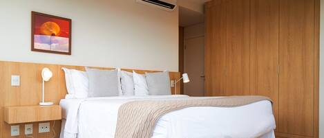 A bedroom with a bed, bedside tables, a lamp, a wall-mounted air conditioner, and a wooden wardrobe.