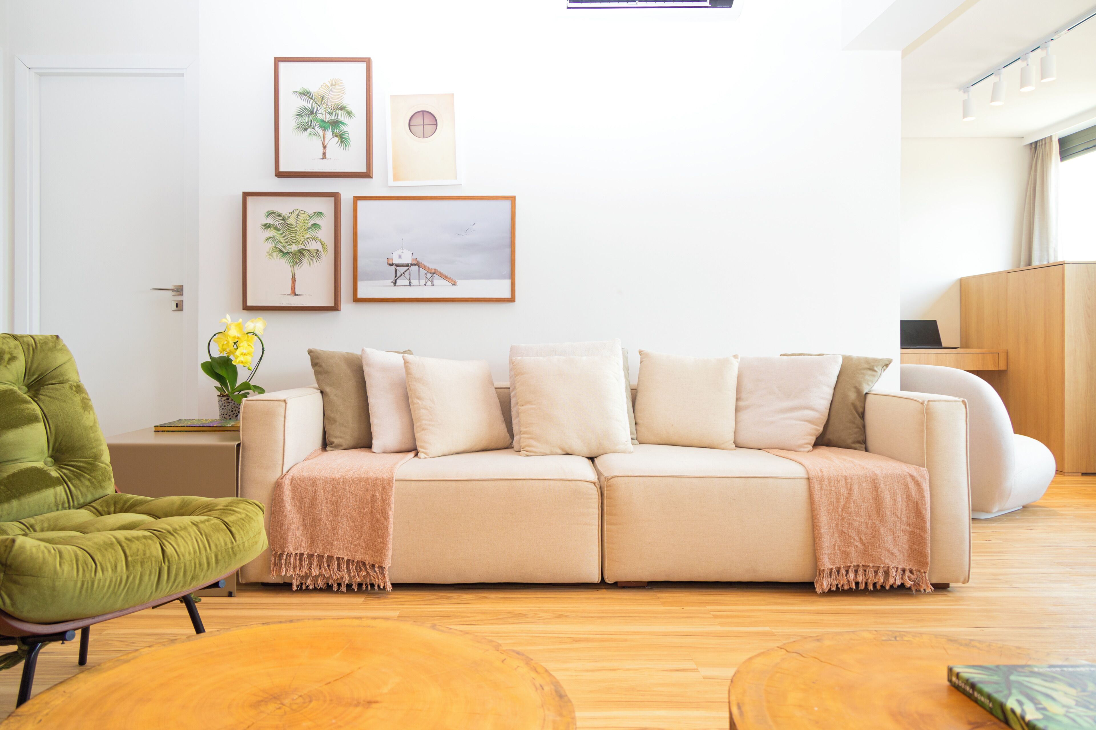A living room with a beige sofa, a green armchair, wooden flooring, and wall-mounted artwork.