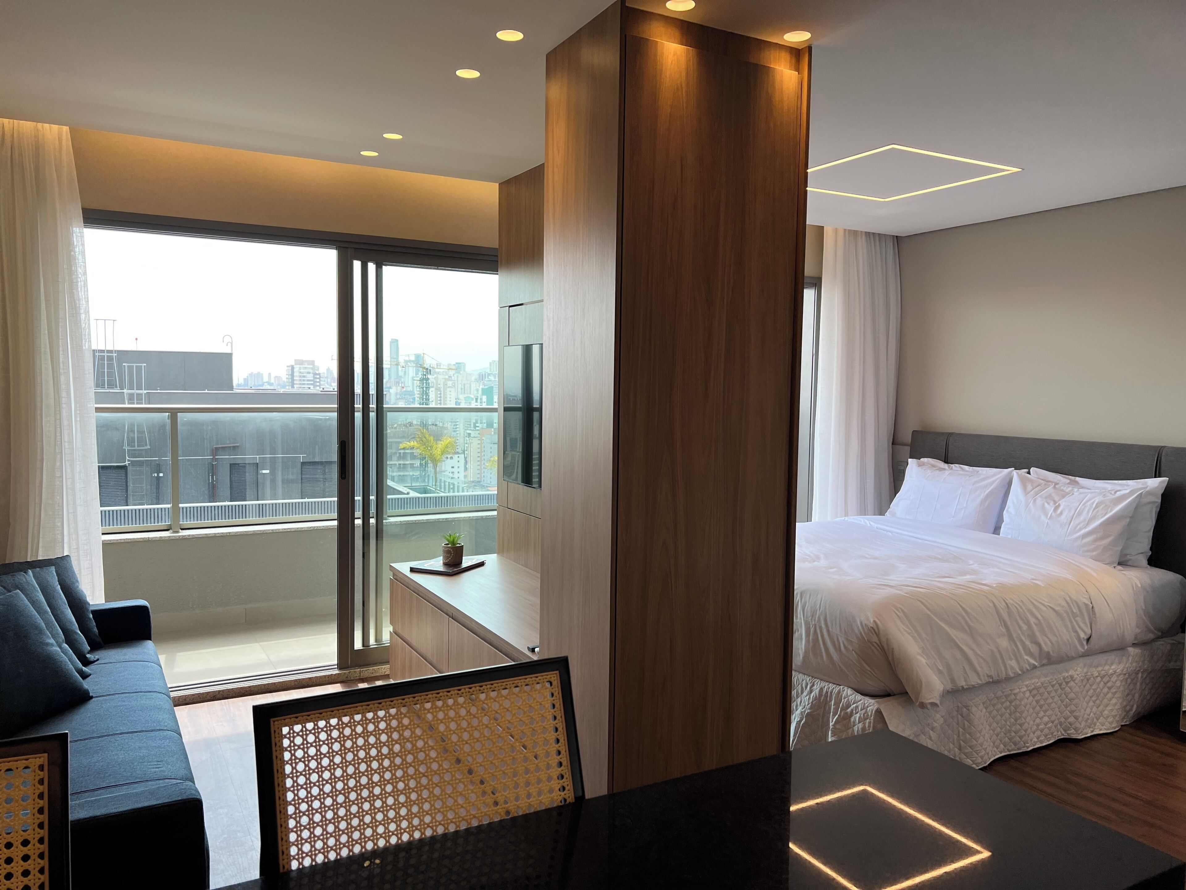 Une chambre d’hôtel moderne équipée d’un lit, d’un canapé, d’un bureau et d’une grande fenêtre donnant sur la ville.