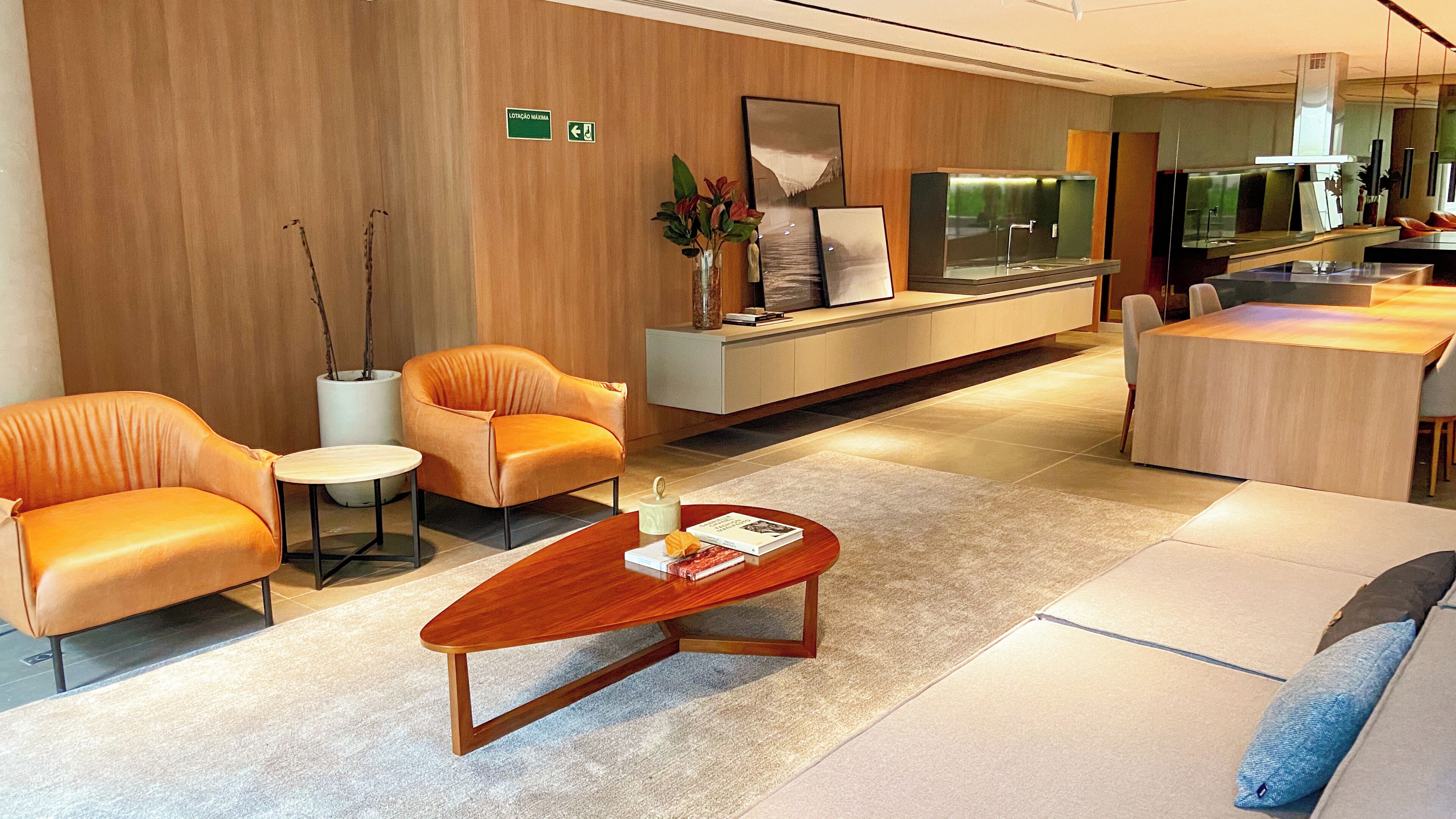 A modern hotel lobby with leather sofas, a wooden coffee table, a reception desk, and a large mirror.