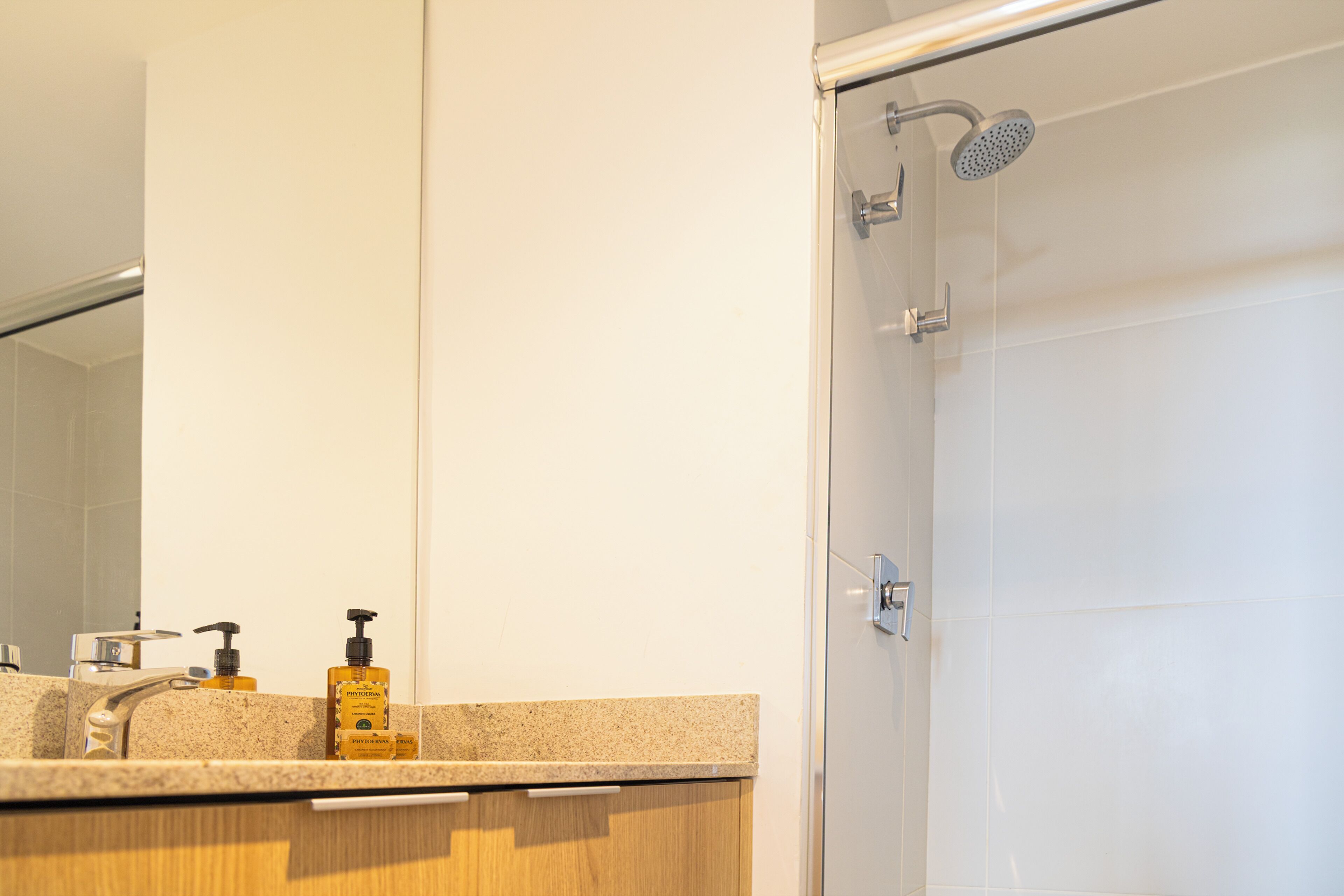 A bathroom with a shower, a sink with a mirror, and two bottles of soap.