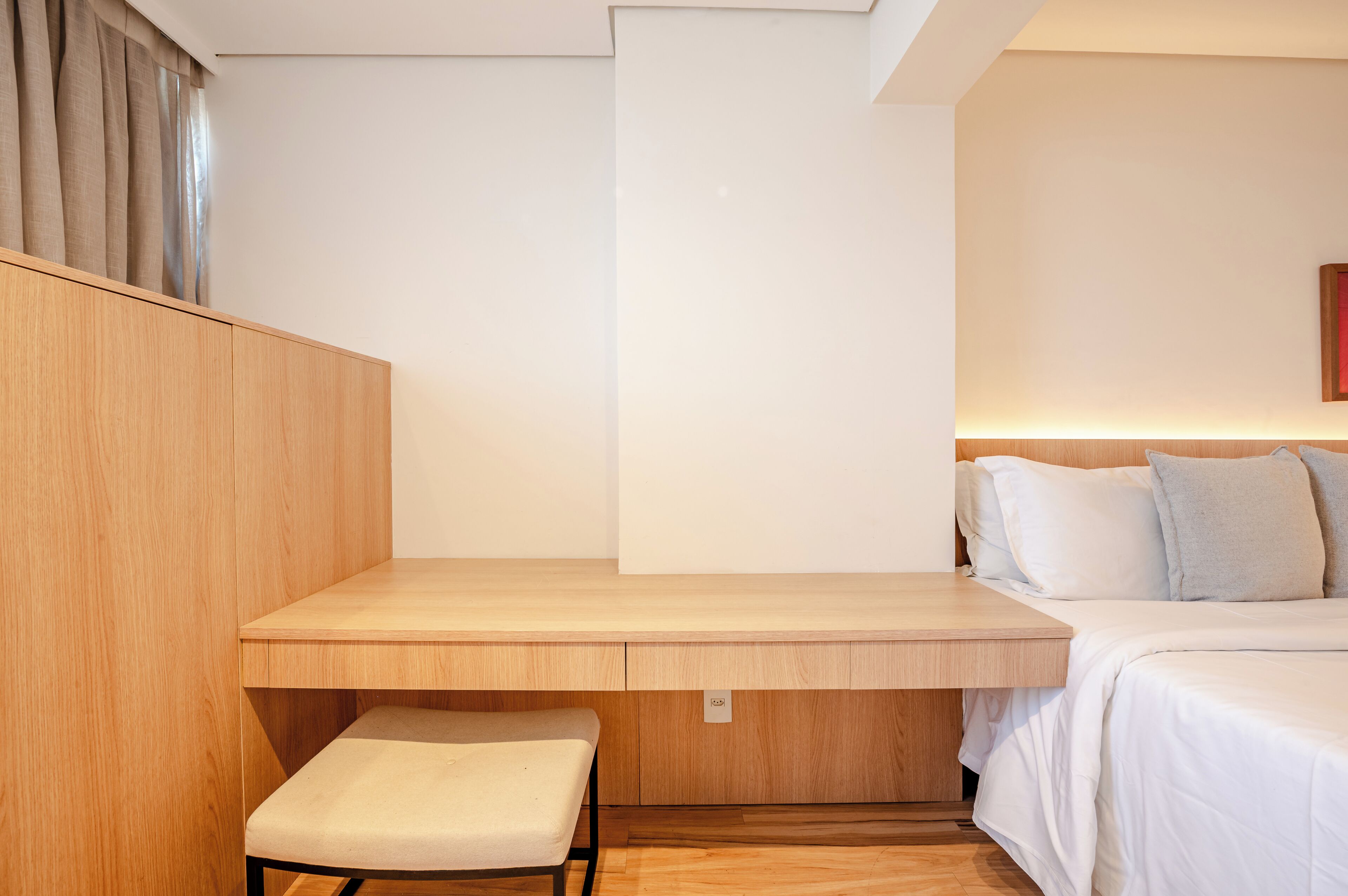 Un dormitorio con un escritorio de madera, un banco, una cama con ropa de cama blanca y un cabecero.