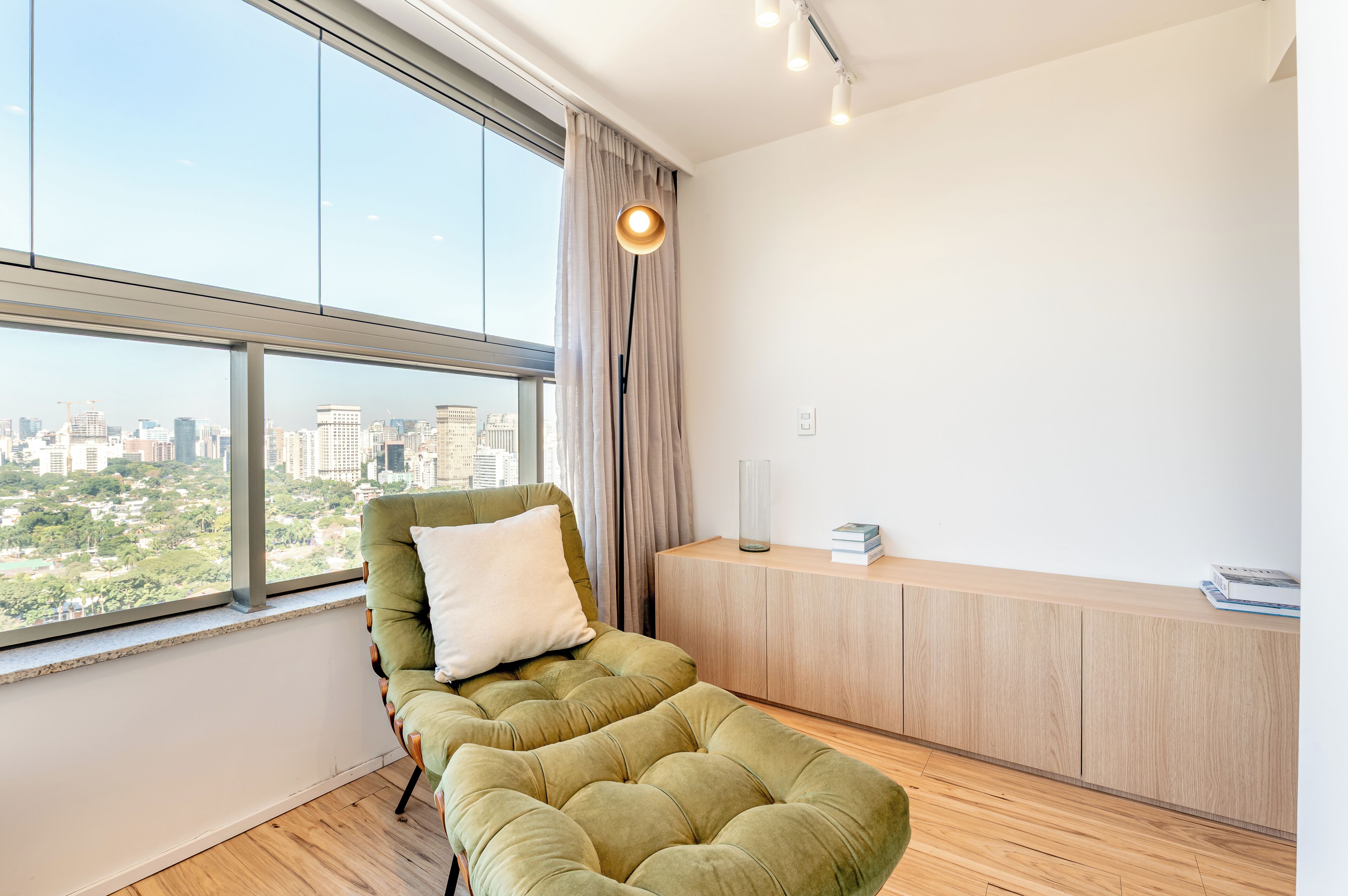 Une pièce moderne dotée d’une grande fenêtre, d’un fauteuil vert à coussins, d’une armoire en bois et d’un luminaire suspendu.