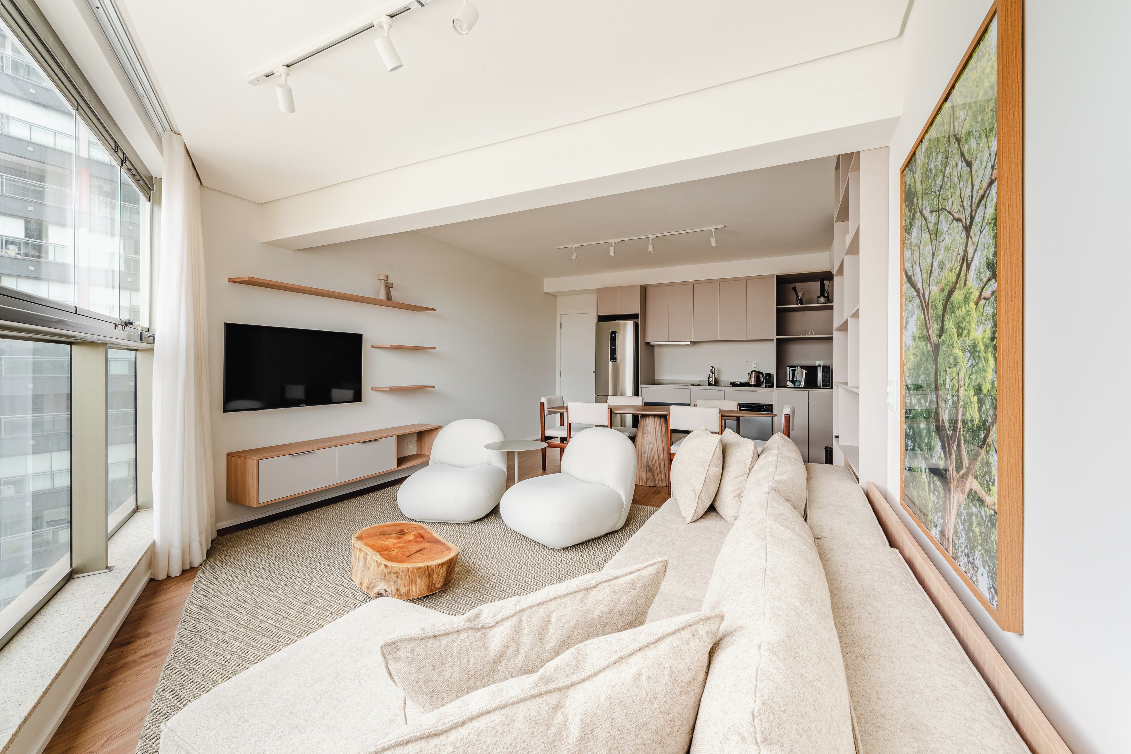 A modern living room with a sofa, chairs, a flat-screen TV, and a kitchen in the background.