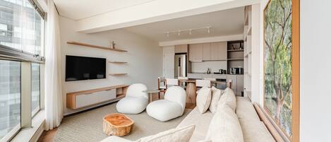 A modern living room with a sofa, chairs, a flat-screen TV, and a kitchen in the background.