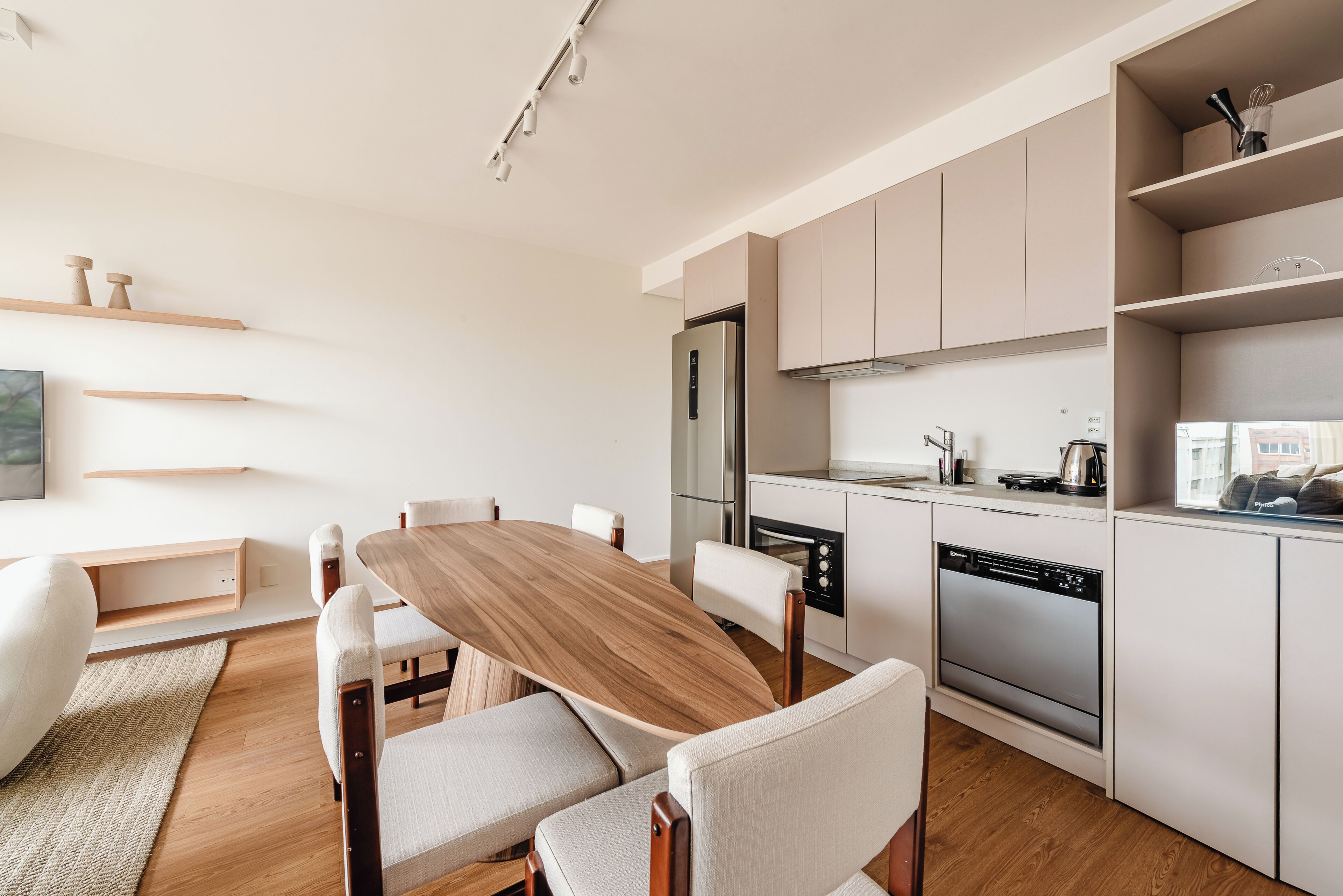 A modern kitchen with a dining area, wooden table, white chairs, and built-in appliances.