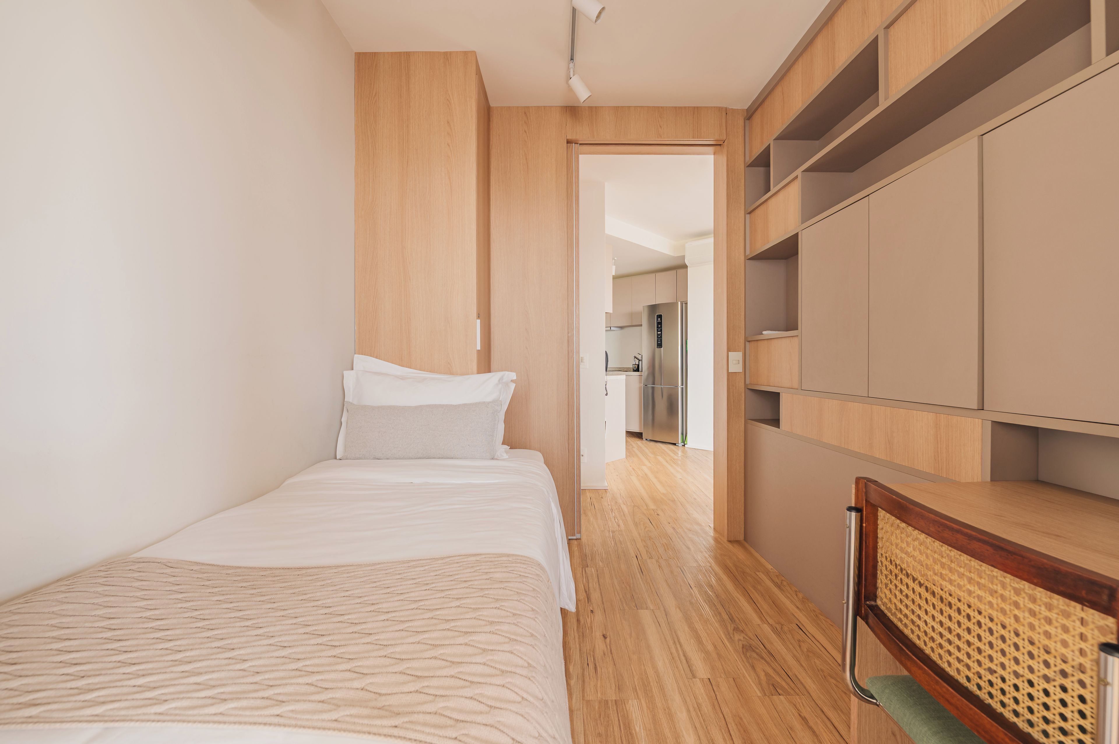 A bedroom with a bed, a wardrobe, and a kitchenette in the background.