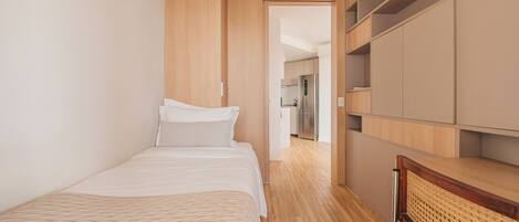 A bedroom with a bed, a wardrobe, and a kitchenette in the background.