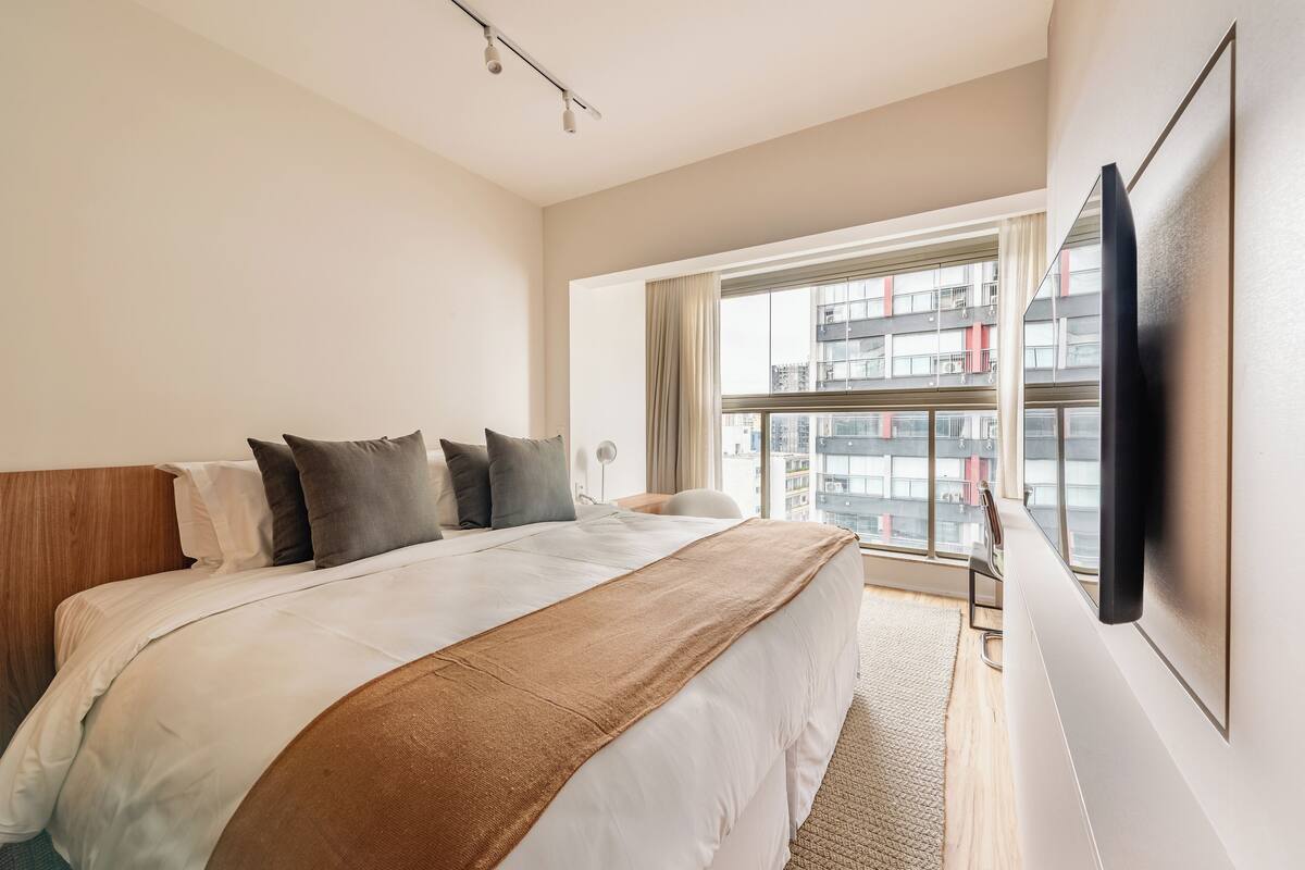 Camera d'albergo con un letto grande, una TV a parete e una finestra vista città.