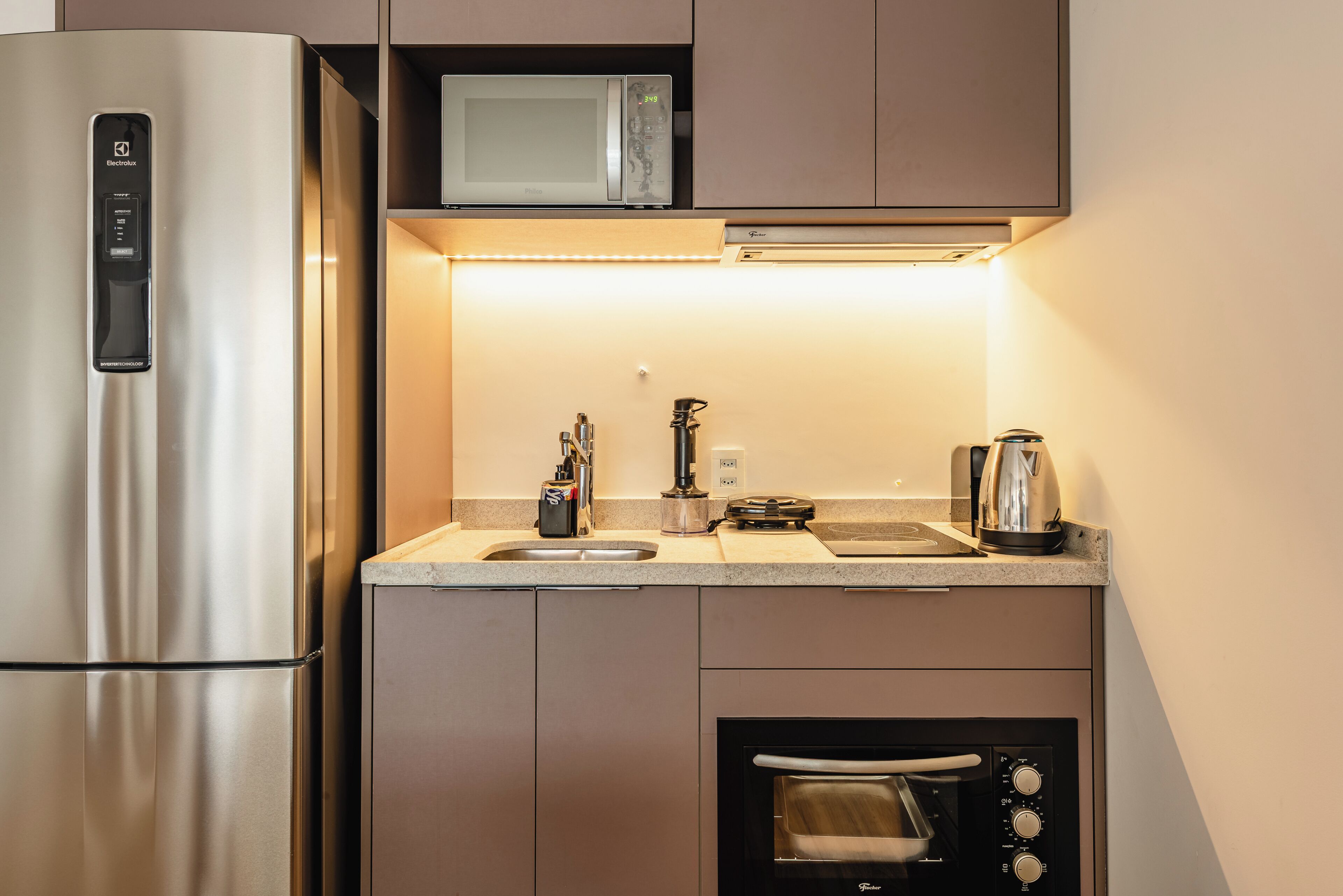 Eine kompakte Küche mit Edelstahl-Kühlschrank, Mikrowelle, Backofen und Kaffeemaschine.
